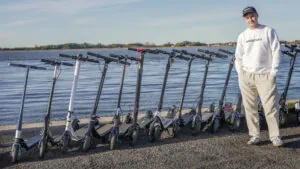 Rasmus from ERideHero next to a wide range of entry-level electric scooters with the ocean in the background